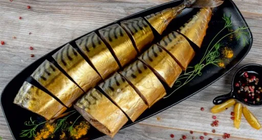Скумбрия холодного копчения, нарезанная кусочками, на тёмной тарелке